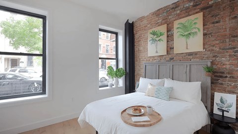 A bedroom with a white bed and a brick wall.