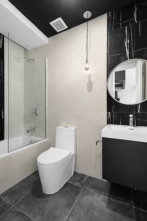 A white toilet sits in a bathroom with a black and white tiled wall.