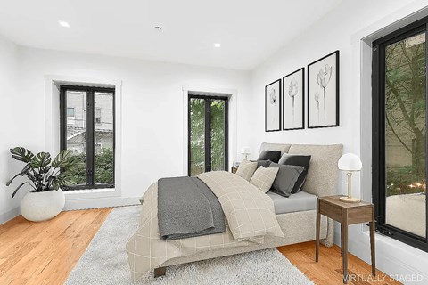 A bedroom with a bed, a potted plant, and a table with a lamp.