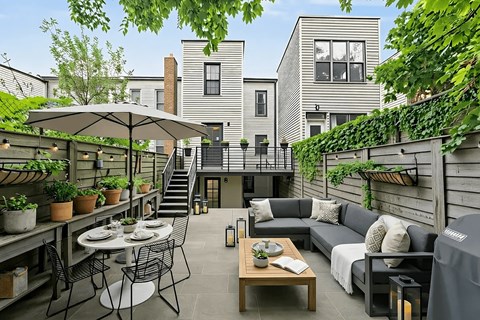 A patio with a table and chairs is surrounded by plants and a building.