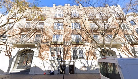 A white van is parked on a street in front of a building with a tree in front of it.