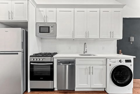A white kitchen with a stainless steel refrigerator, oven, dishwasher, and washing machine.