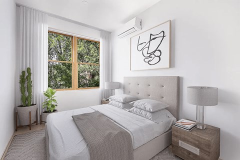 A bedroom with a large bed, a nightstand with a lamp, and a window with a view of trees.