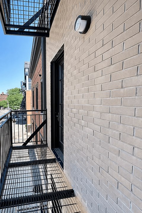 A brick wall with a black gate and a small square light fixture on it.