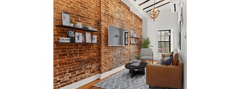 A living room with a brick wall and a brown couch.