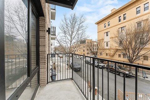 A balcony with a black railing and a view of a parking lot and buildings.