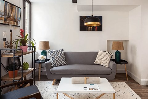 A living room with a grey couch, a white coffee table, and a black side table with a lamp.