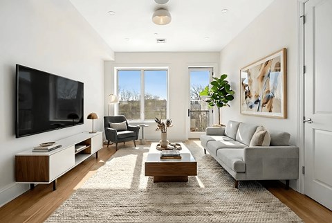 A modern living room with a grey sofa, a wooden coffee table, and a large flat-screen TV mounted on the wall.