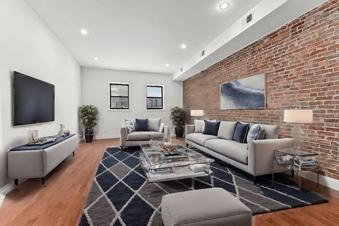 A living room with a grey couch, a black television, and a brick wall.