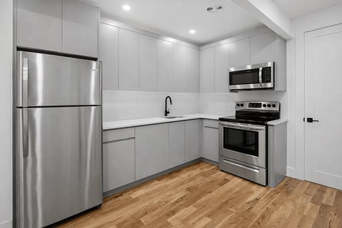 A modern kitchen with a stainless steel refrigerator and wooden flooring.