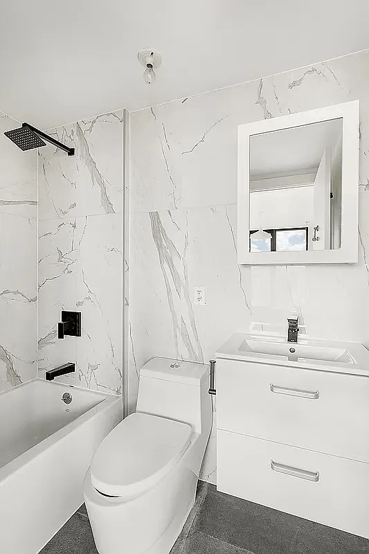A white bathroom with a marble wall and a round toilet.
