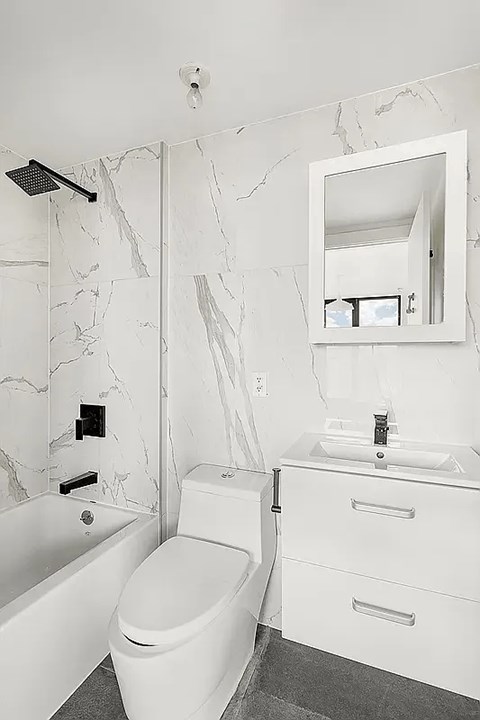 A white bathroom with a marble wall and a round toilet.