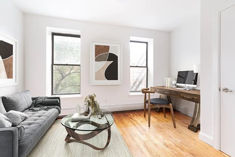 A modern living room with a grey couch, a glass coffee table, and a wooden desk with a laptop.