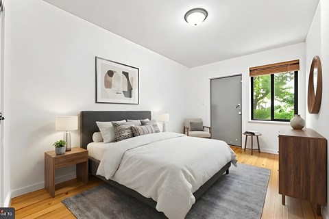 A bedroom with a large bed, a nightstand, a chair, and a window.