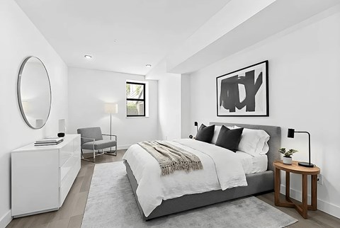 A modern bedroom with a large bed, a chair, a dresser, and a mirror.