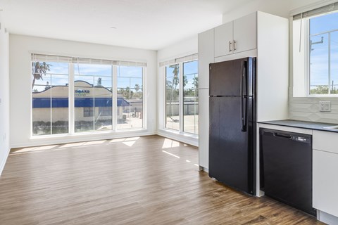 A black refrigerator sits in a kitchen with wood floors and white walls.