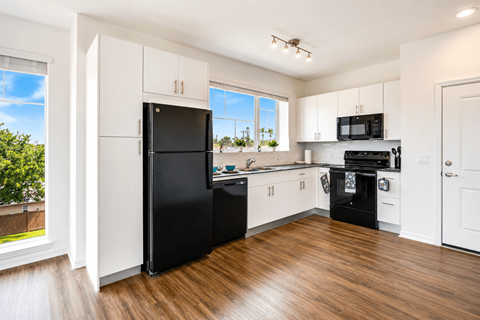 A black fridge and oven in a white kitchen with wooden floors.