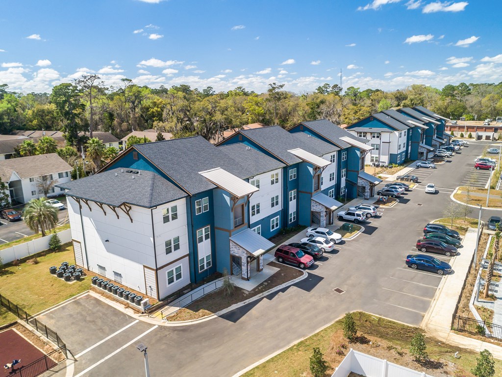 an aerial view of a row of multifamily buildings with a parking lot and trees in the