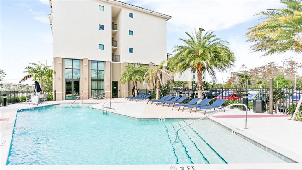 a large swimming pool with blue chairs and a building in the background