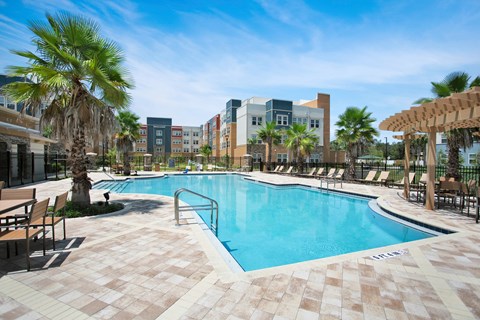 A pool surrounded by palm trees and lounge chairs.