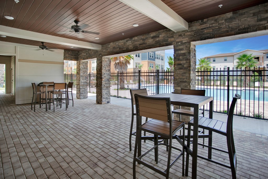 a patio with tables and chairs and a pool in the background