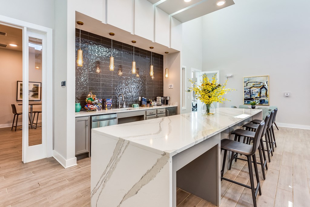 a kitchen with a large white island with a long countertop and a row of black chairs