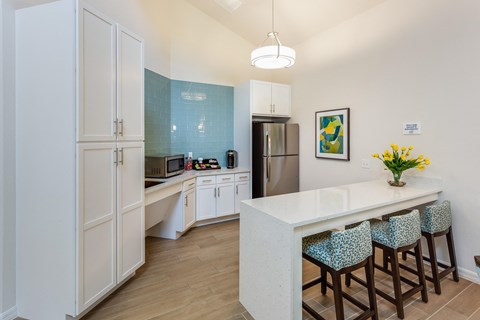 A kitchen with white cabinets and a white island with blue chairs.