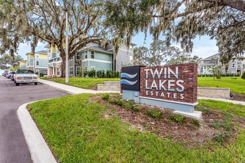 A sign for Twin Lakes Estates is in front of a grassy area.