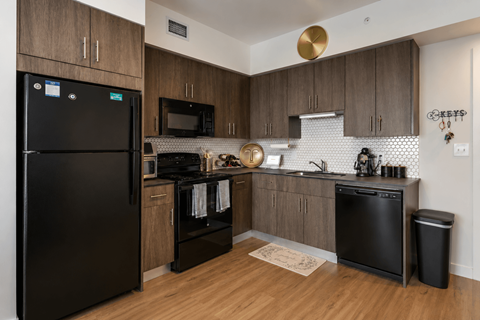A black fridge sits in a kitchen with wooden cabinets and a black dishwasher.