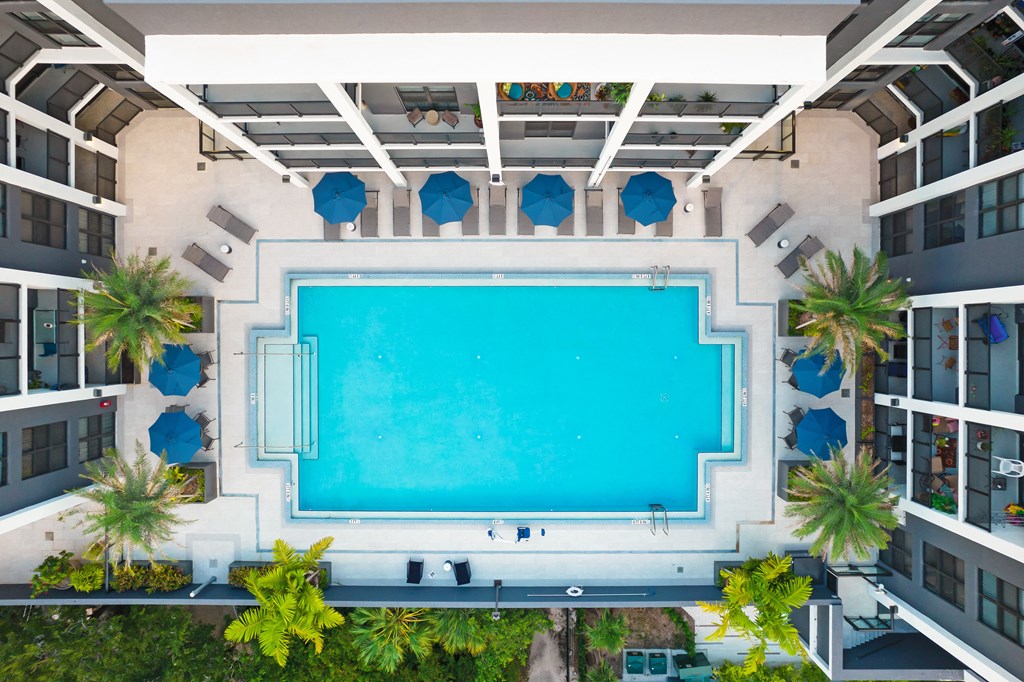 an overhead view of a swimming pool with blue umbrellas and palm trees