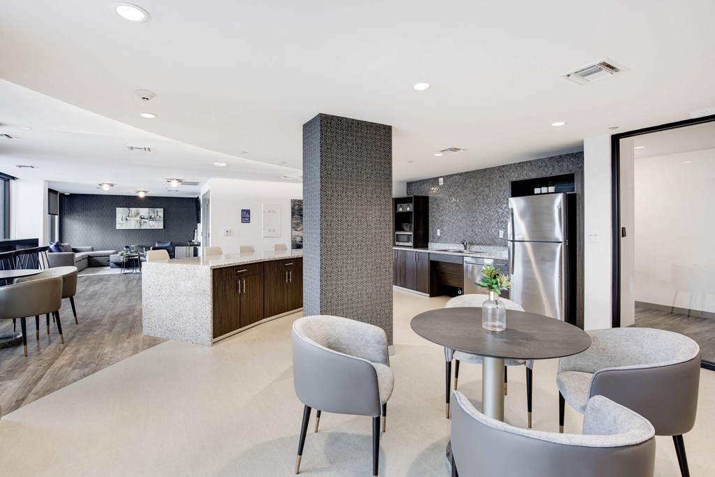 a room with a table and chairs and a kitchen in the background