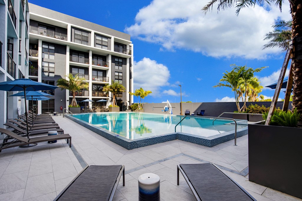 a large swimming pool with lounge chairs and umbrellas in front of a hotel