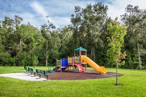 A playground with a yellow slide and green benches.