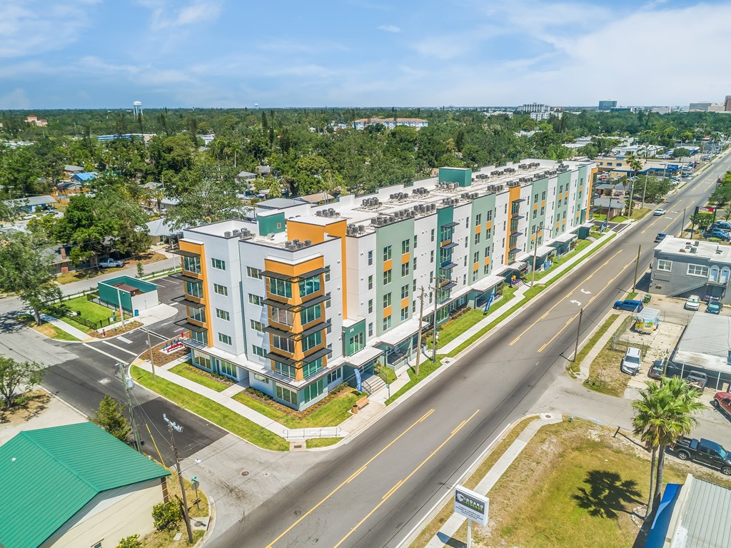 A multi-story apartment building with a green roof is surrounded by a road and other buildings.