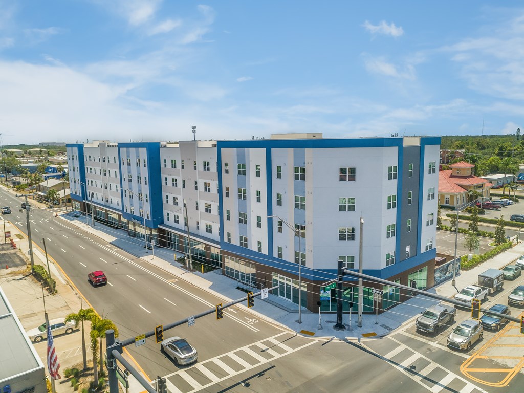 A large white and blue building is situated on a street corner with cars and a traffic light.