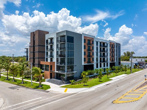 A modern multi-story building with a parking lot in front.