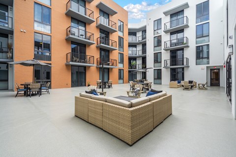 A large wicker sofa sits in the middle of a courtyard with buildings in the background.