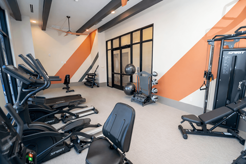 A gym with orange walls and a variety of exercise equipment.