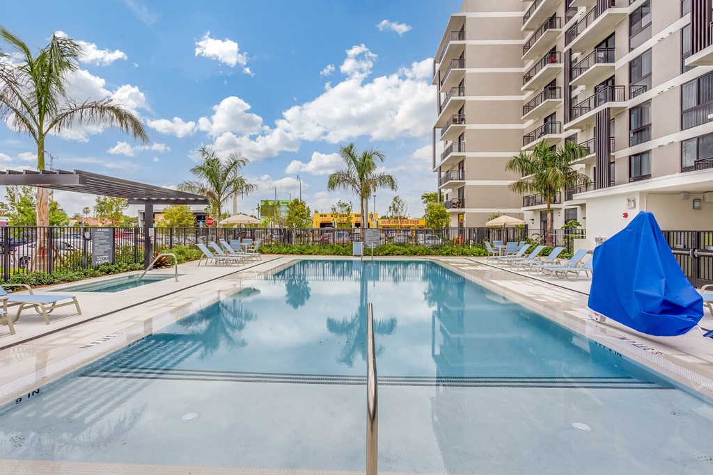 A large swimming pool in front of a building with a blue umbrella on the right side.