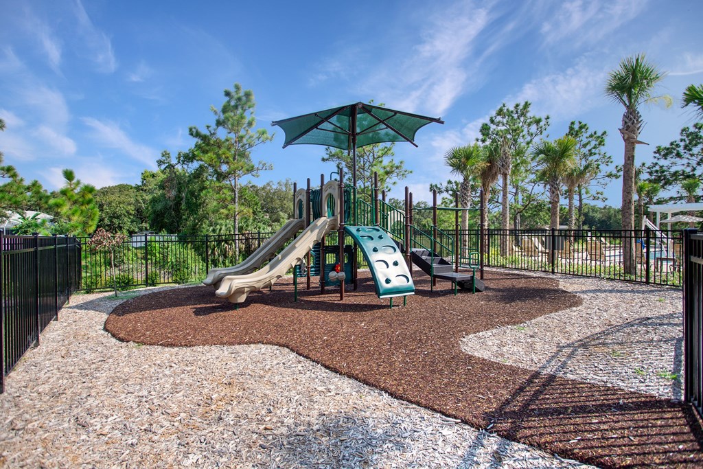 A playground with a green umbrella and a slide.