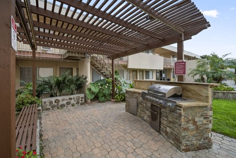 A patio with a grill and a pergola.