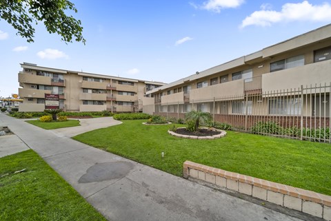 A concrete pathway leads to a grassy area in front of apartment buildings.