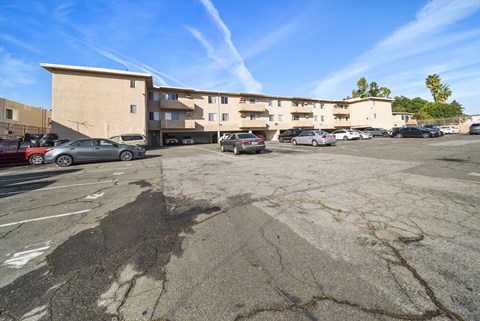 A parking lot with a building in the background and several cars parked.