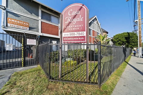 A sign for Casa Royale Apartments is displayed in front of a fence.