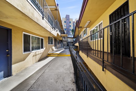 A long, narrow balcony with black railings and a yellow wall.