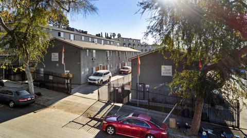 A red car is parked in front of a building with a black fence.