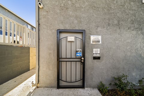 A black gate with a blue sign that says "OPEN" in front of a grey wall.