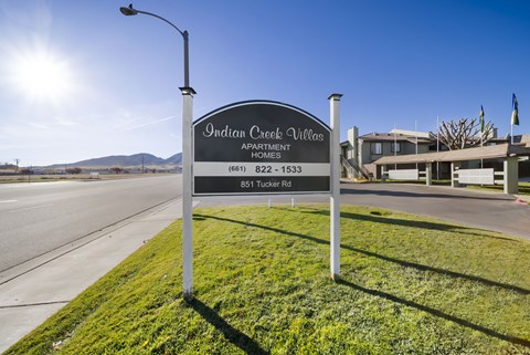 A sign for Indian Creek Village Apartment Homes stands on a grassy area by a road.