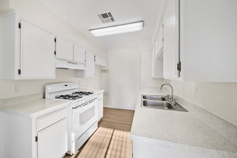 A white kitchen with a stove, sink, and cabinets.