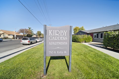 A sign for Kidby Gardens Apartments stands in the grass by a road.